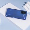 Product shot of blue Huawei nova Y70 Plus against a blue background with white objects next to it