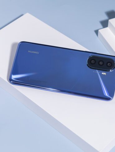 Product shot of blue Huawei nova Y70 Plus against a blue background with white objects next to it