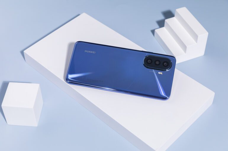 Product shot of blue Huawei nova Y70 Plus against a blue background with white objects next to it