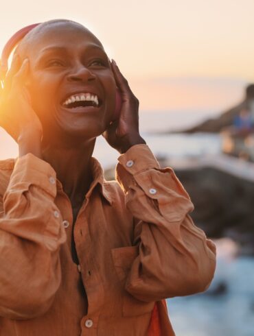 Image of a person listening to music with wireless headphones and a beautiful sunset is in the background