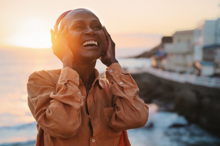 Image of a person listening to music with wireless headphones and a beautiful sunset is in the background