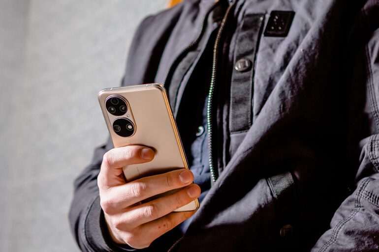 HUAWEI P50 - Lifestyle - Image of a person wearing black clothing holding a gold Huawei P50 in their hand