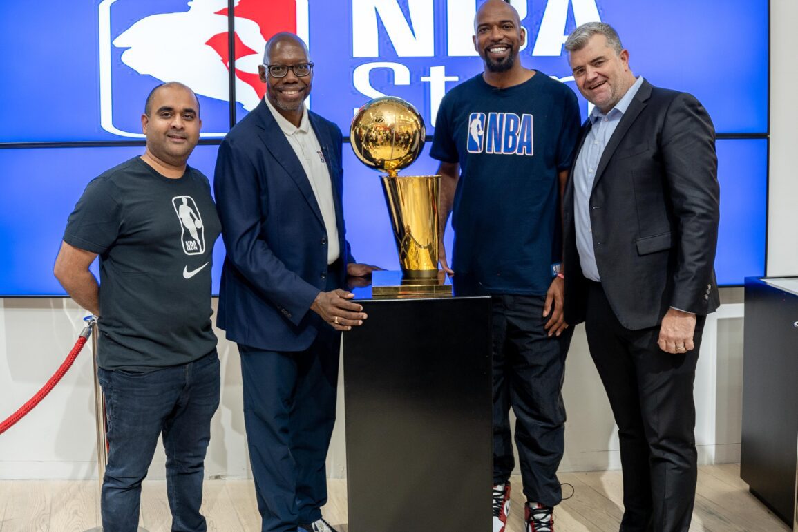 Group image of NBA Africa CEO Victor Williams, Shesha CEO Nirmal Devchand and 2004 NBA champion Richard “Rip” Hamilton in front of an NBA sign with an NBA trophy at the opening of the first NBA store in Africa