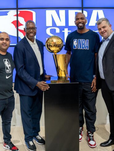 Group image of NBA Africa CEO Victor Williams, Shesha CEO Nirmal Devchand and 2004 NBA champion Richard “Rip” Hamilton in front of an NBA sign with an NBA trophy at the opening of the first NBA store in Africa