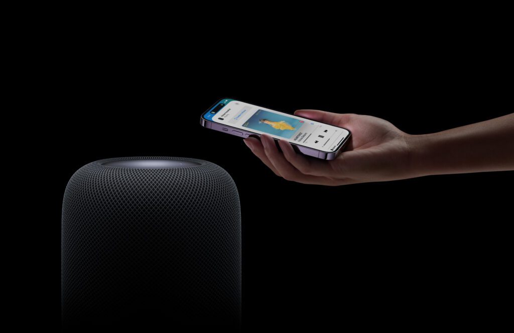 An image of the new Apple HomePod with a person's hand holding an iPhone 14 Pro demoing the handoff feature